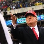 A man in suit and red hat throws coins in the stadium.