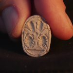 Two fingers holding an ancient amulet.