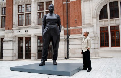A black man looks at a sculpture of a tall black woman.
