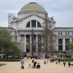 People stand on tall, classic-style museum buildings with columns.