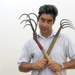 A man holding two rakes on his chest.