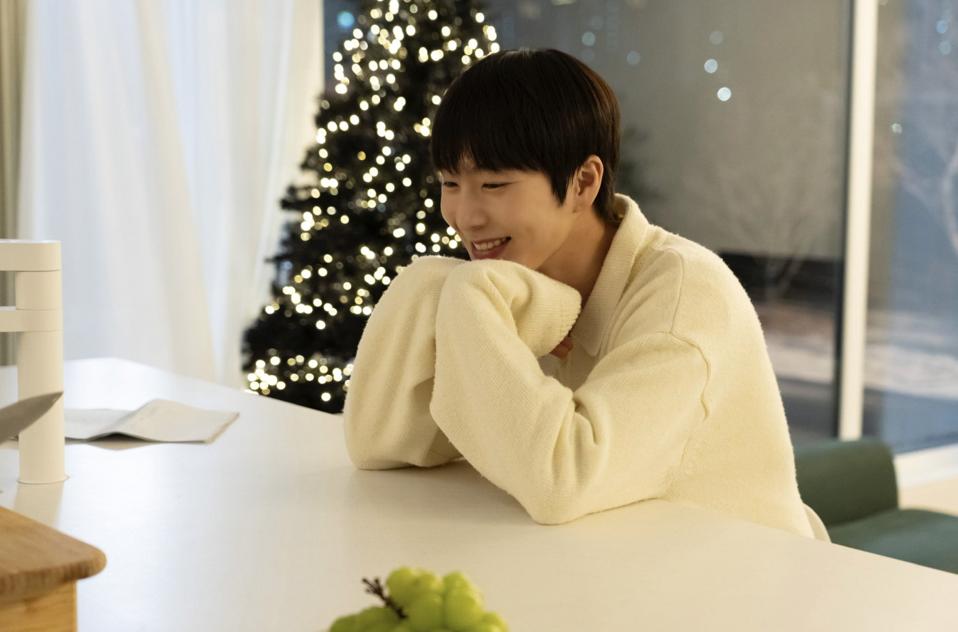 A smiling young man sitting on the counter in front of a Christmas tree.