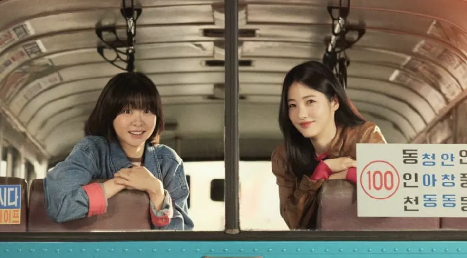 Two young women looking at the rear window of the Korean bus.